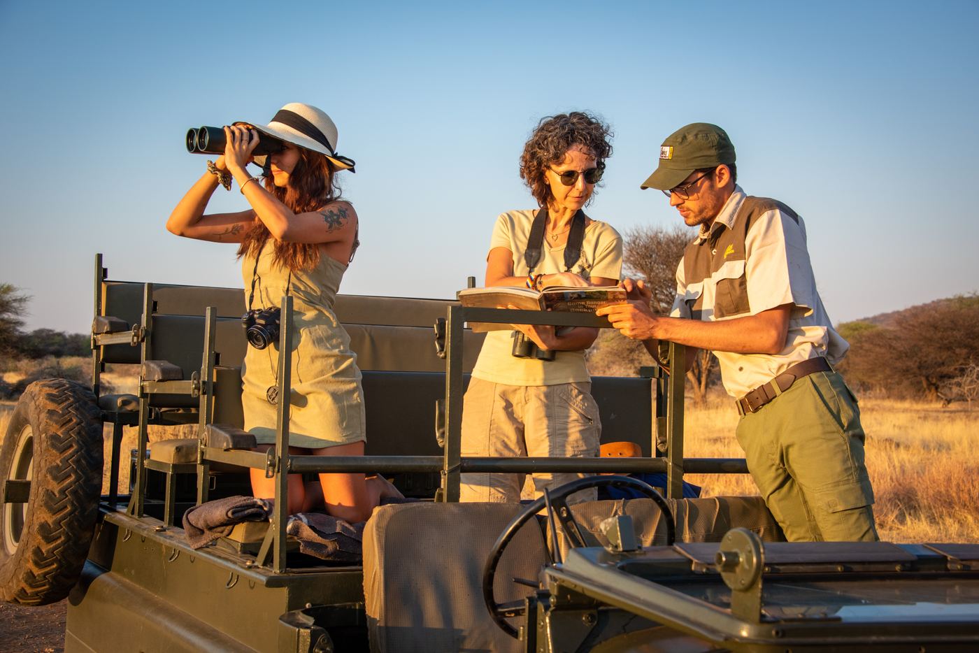 A guide and two guests on an open safari vehicle discussing a sighting